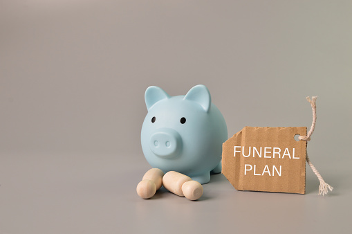 Piggy bank, people figures and label tag written with FUNERAL PLAN