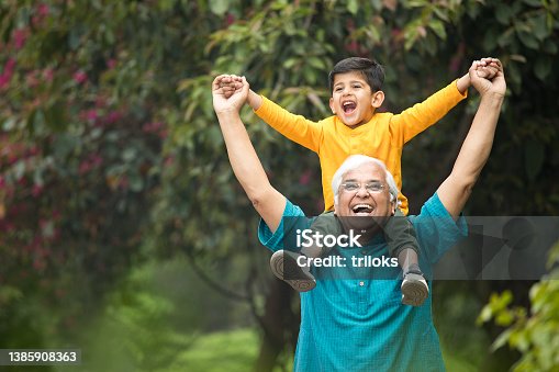 istock Old man carrying grandson on shoulders at park 1385908363