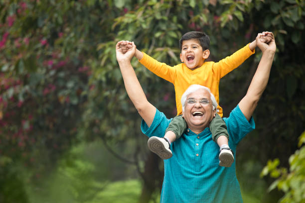 Old man carrying grandson on shoulders at park stock photo