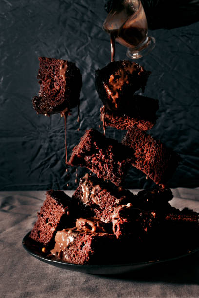 Pieces of chocolate cake in the air, liquid chocolate is pouring for dessert, on a black background, dark style photo, flying food and baking levitation stock photo