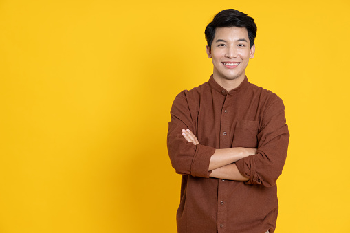 Joven asiático sonriente con los brazos cruzados en un estudio amarillo de fondo aislado photo