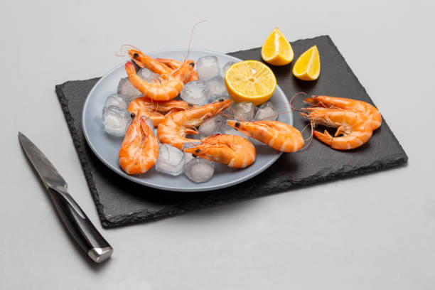 istock Shrimps, lemon and ice on a gray plate and on a stone surface. 1385912748