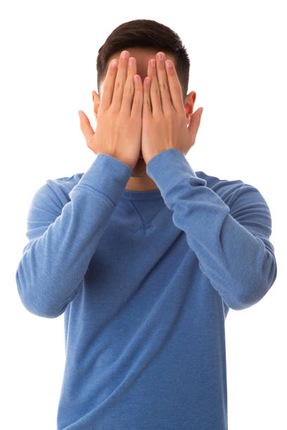 Teenager wearing blue hiding from embrassment on cut out white background