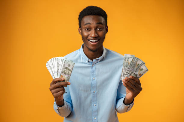 istock Excited black guy holding stack of Dollars in yellow studio 1385915972