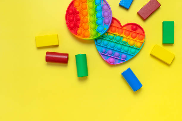 istock Popular silicone multi-colored anti-stress toy pop it and wooden constructor on yellow background flat lay top view. Trendy modern sensory children's toy, fidget push pop it 1385916625