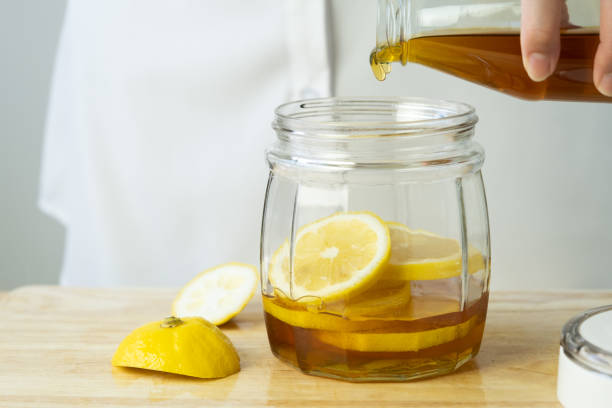 istock woman's hand pouring honey in a clear jar with lemon 1385917026