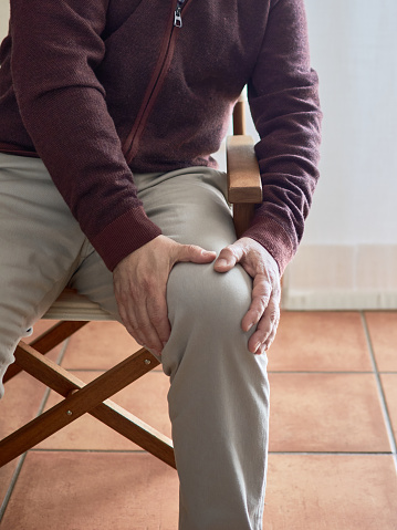 A middle-aged man has to sit massaging his knee because it hurts a lot due to osteoarthritis or arthritis.