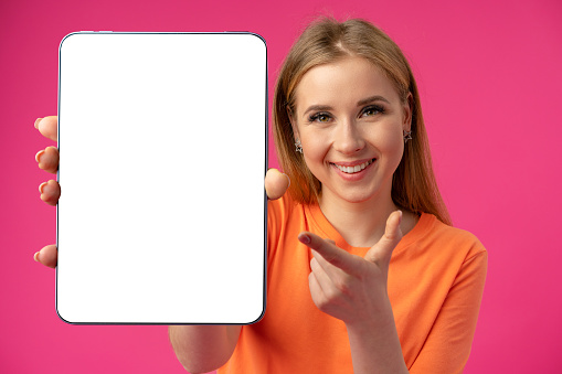 Young smiling woman showing digital tablet with blank screen against pink background, close up