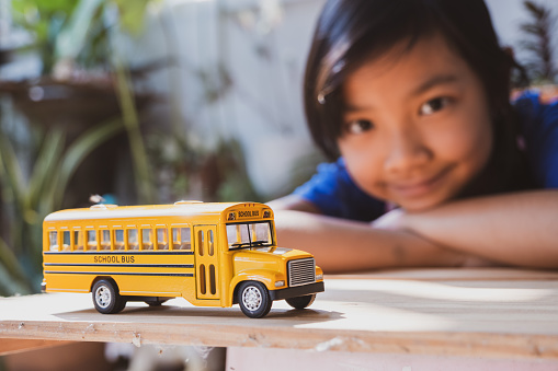 Asian girl playing yellow school bus model at home smiling happy to go to school