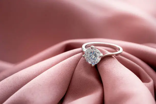 The wedding diamond ring is placed on a pink gold cloth.