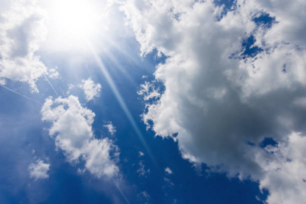 Beautiful blue sky with white cumulus clouds and sun rays (sunbeams). Backlight photography.