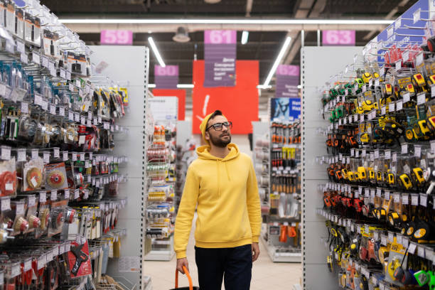 un client avec un panier d’achat se promène dans un hypermarché de construction et examine la gamme de produits - heavy plant photos et images de collection