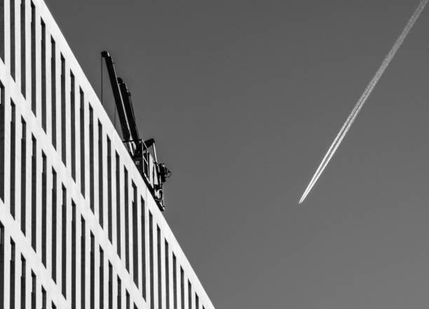Airplane trail forming a V shape with modern office building and a crane. Black and white.