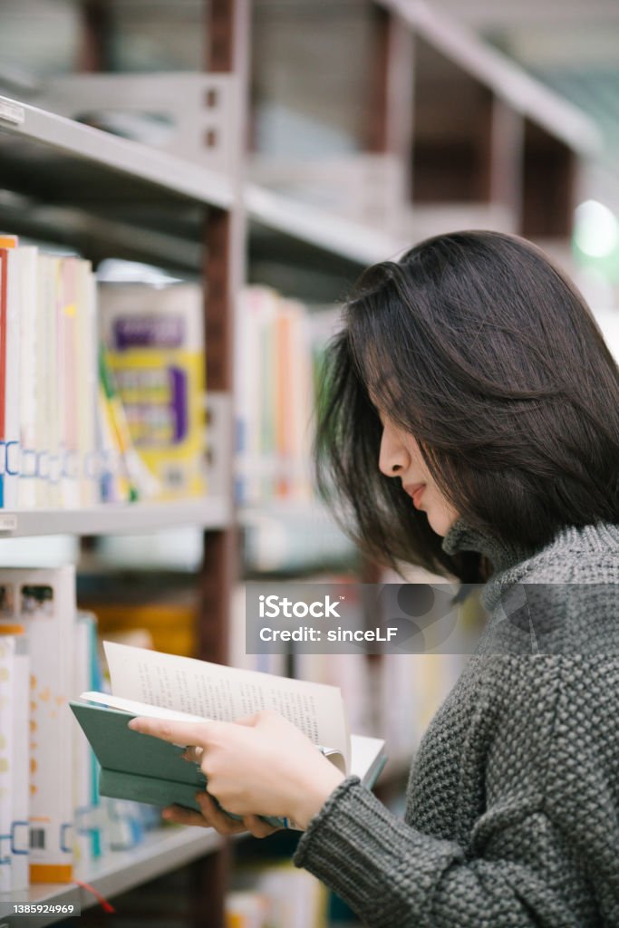 Asian female students choose books from bookshelves in the library Picking book from bookshelf Library Stock Photo