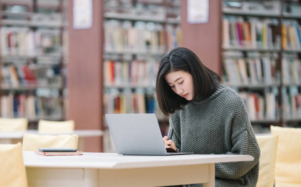 istock Asian female students study by themselves on laptops in the library 1385925080
