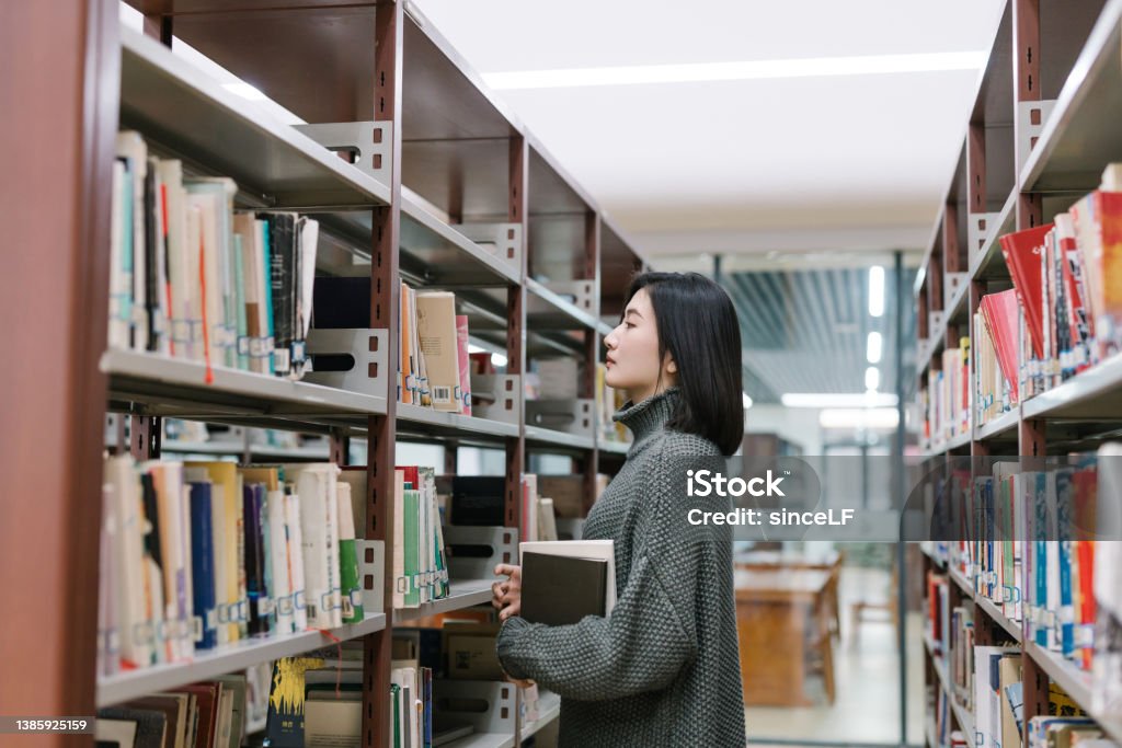 Asian female students choose books from bookshelves in the library Picking book from bookshelf 20-24 Years Stock Photo