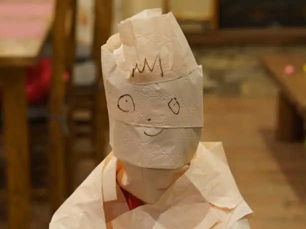 Children play. Pretty girl is wrapped in toilet paper like a mummy. The face is drawn with a felt-tip pen. Theme of childhood and leisure at home.