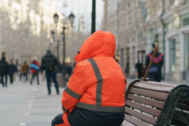 Moscow, Russia - March 19, 2021: Famous pedestrian touristic Nikolskaya street in spring day. Municipal tired janitor resting at the bench. He looking at the Red Square side of the street. Back, rear view.