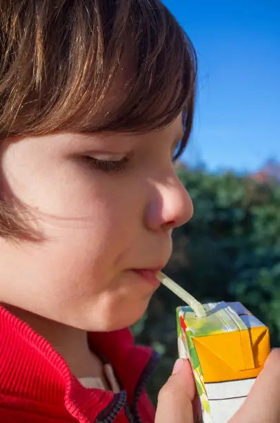 Photo of Child boy drinking sweetened juice fruit juice from brick