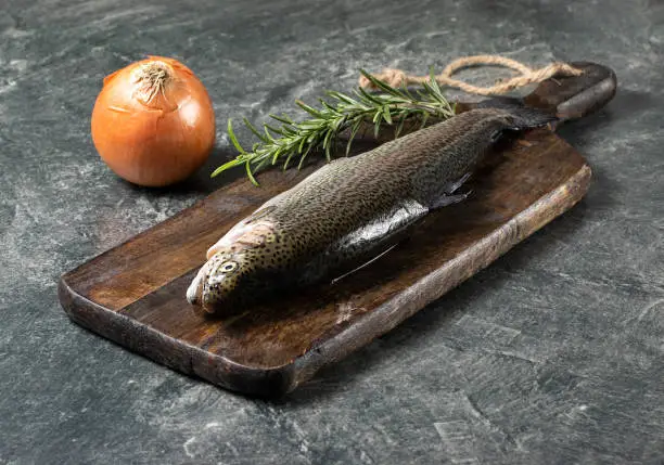 Raw trout with rosemary and onion on a grey background, wooden vintage board, isolated, healthy eating concept, fish. Stock photo