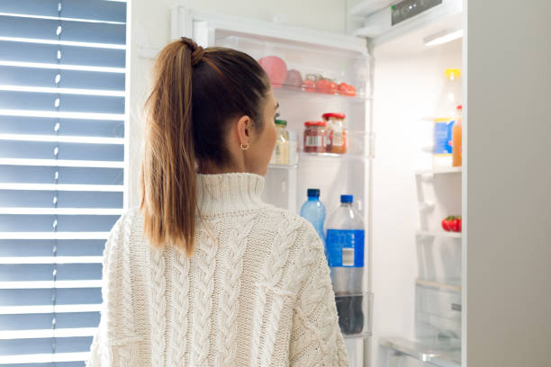 istock Young woman in a sweater peeks into the refrigerator 1385934470
