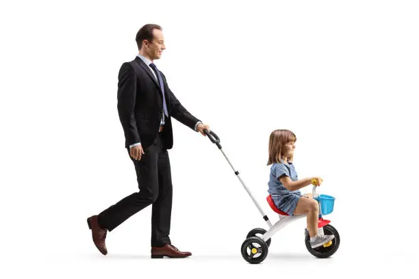 Photo of Profile shot of a father pushing a girl on a tricycle