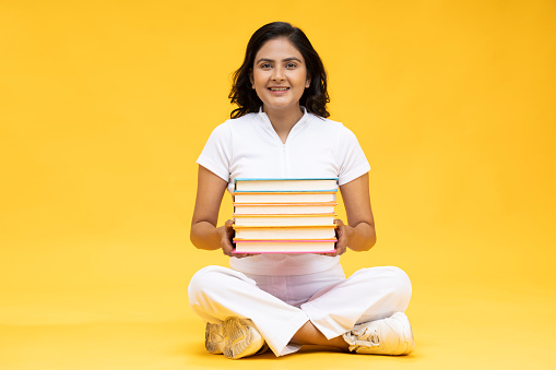 Portrait of a young girl holding book, yellow background