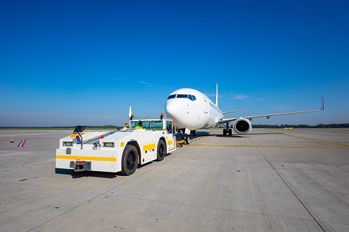 The aircraft towing system at the airport. Man driving a pushback tractor attached to plane nose. Wide angle view.