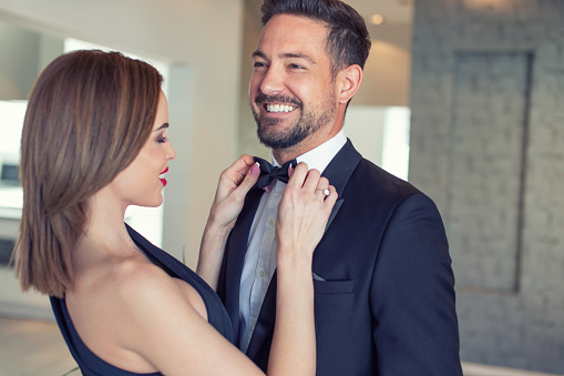 Young elegant Caucasian woman adjusting bow tie for successful man, preparing for night event