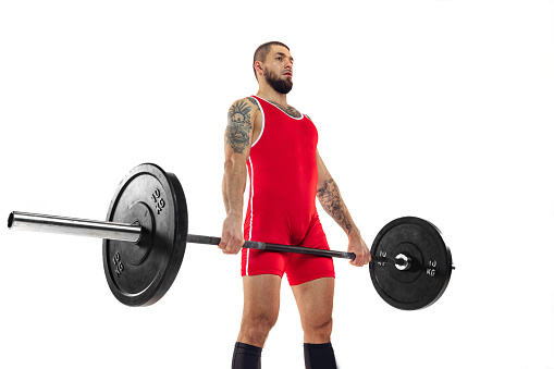 Close-up strong man red sportswear raising barbell up isolated on white background. Young bearded muscular athlete with tattoo on his body training with barbell. Sport, weightlifting, achievements concept