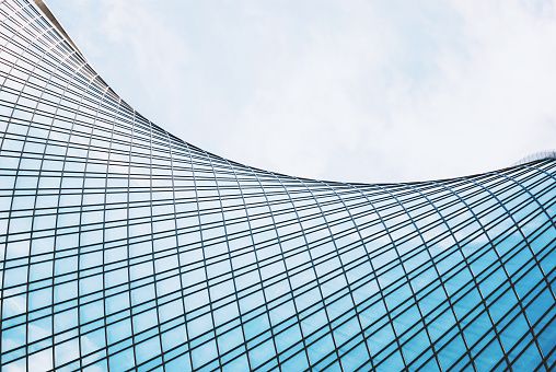 Blue glass and pyramids pattern on a commercial building façade - curtain walls form the outer shell of a building and stands as a separate shell in front of the actual supporting structure. They usually runs across the floors. Since the wall only supports its own weight and no other static loads from the building, it can be designed as a lightweight structure. The curtain wall is attached or suspended from the building's supporting structure using a substructure. The façade spanning several floors usually has a frame construction made of steel or aluminum profiles, which is largely filled with glass or other flat filling elements.