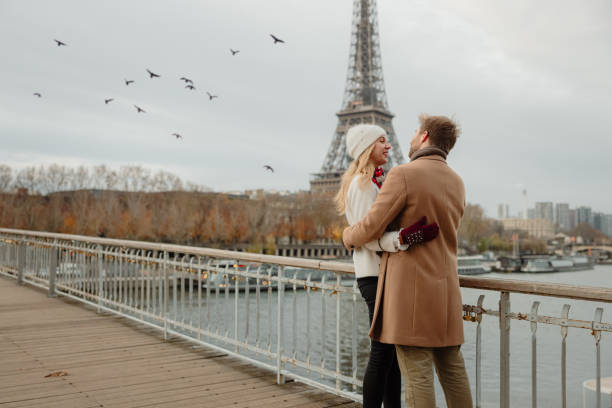 Romantic couple hugging each other closely while standing on a bridge at Seine River with Eiffel tower, Paris, in background