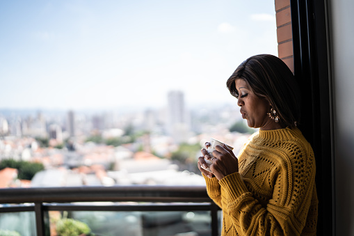 Woman drinking coffee or tea at apartment's balcony