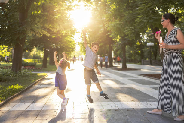 istock Mother standing in park and blowing bubbles with bubble wand while two kids catching them 1385946543