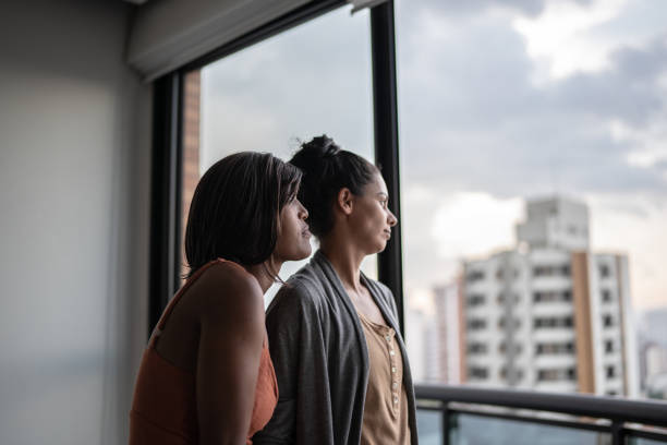 istock Contemplative lesbian couple looking through window at home 1385946898