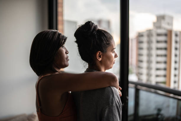 istock Contemplative lesbian couple looking through window at home 1385946900