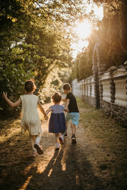 istock Back view of three kids while holding hands and running on footpath 1385946986