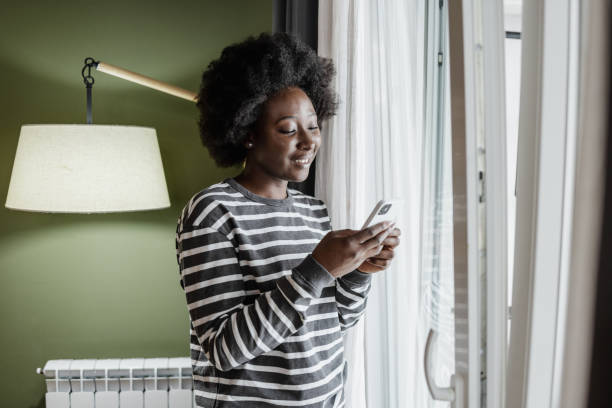 istock A young African-American woman using a mobile phone by the window 1385949635