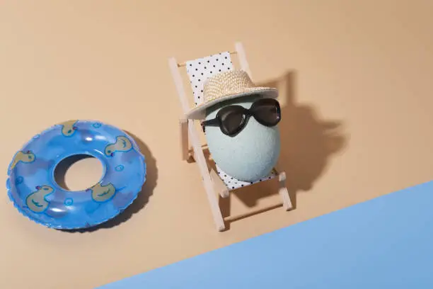 Photo of A cheerful Easter composition with an egg in sunglasses lies on a sun lounger on the beach