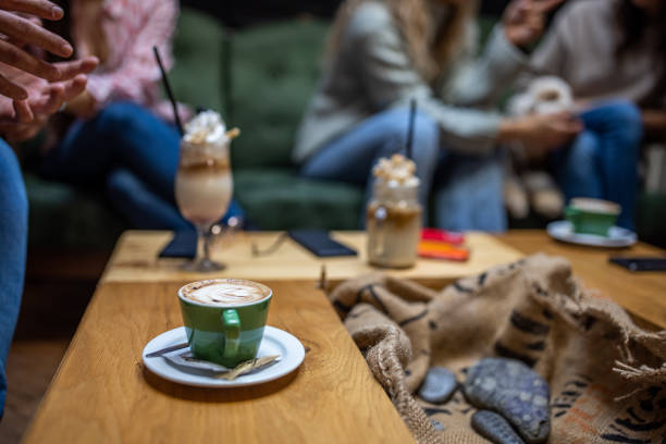 Focus on cappuccino on the table at the coffee shop, while in background young friends talking