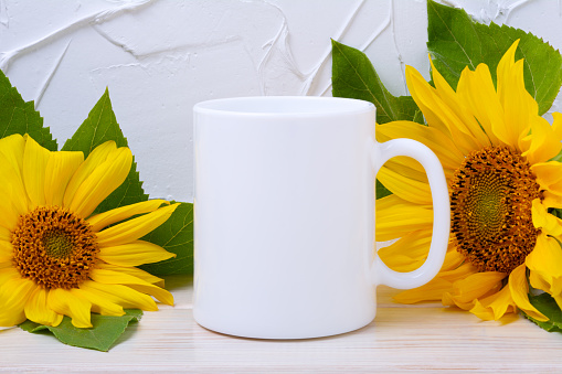 White coffee mug mockup with two sunflowers on the wooden table. Empty mug mock up for design promotion, styled template