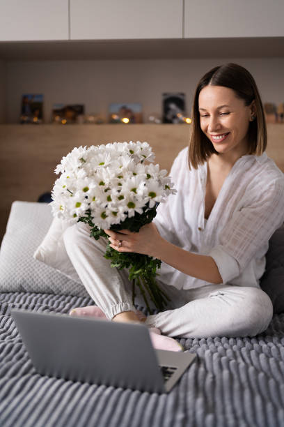 istock Woman communicating using a laptop while stating on bet with a bunch of white flowers 1385951871