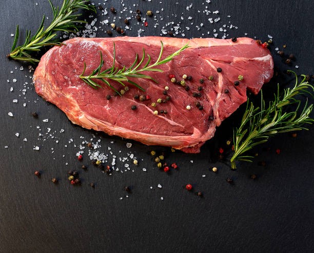 istock Raw beef steak with spices and rosemary on a dark background. Top view with copy space. 1385951948