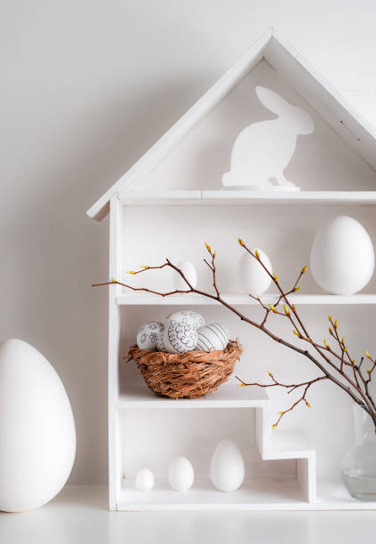 istock Home minimalist interior with Easter decor. Branches with budding buds in a glass vase on shelves in the shape of a house, 1385952138