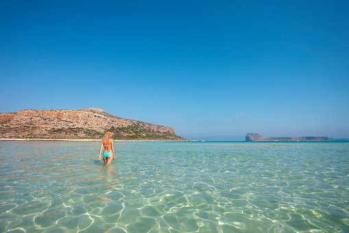 Cheerful woman enjoying walking in shallow water in sea. She is in turquoise water by the Balos beach on Crete island.