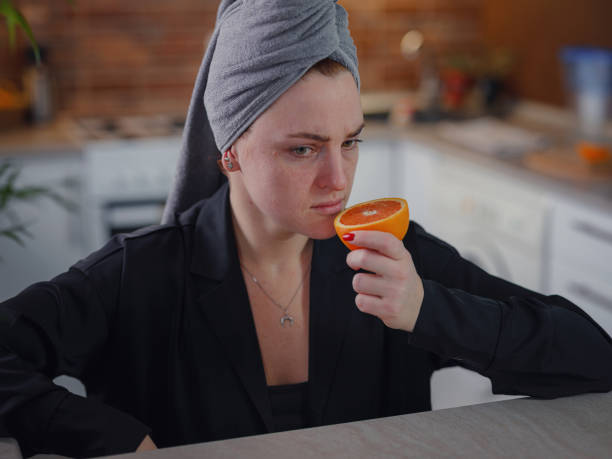 Sick woman trying to sense smell of fresh orange Sick woman trying to sense smell of fresh orange, has symptoms of Covid-19, corona virus infection. Long-lasting covid19 symptom. Loss of taste of food. Loss of smell as one of long-term sars-cov-2 effects. long covid stock pictures, royalty-free photos & images