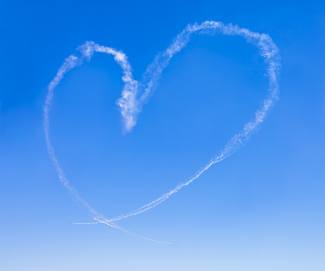 White smoke of heart shape in a clear blue sky, the imagination of airplane engine trace display with copy space. Symbol of romance, drawing of love floating in the air at a romantic moment concept.