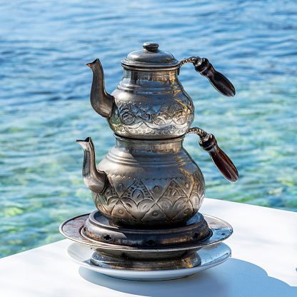 The teapot decorated with traditional Turkish motifs is on the warmer. In the background, the sea appears out of focus.