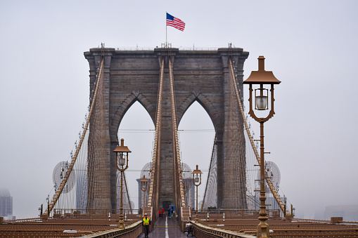 People are seen walking across Brooklyn Bridge in New York City on a foggy day, March 17, 2022.