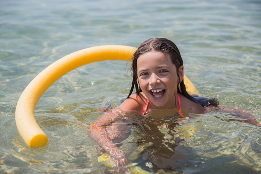 Cheerful teenager smiling when swimming with woggle in the sea water